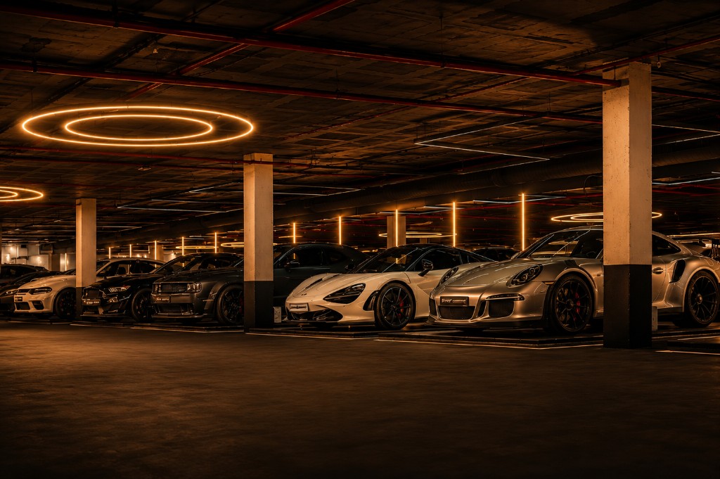 Supercars including Porsche 911 GT3 RS and McLaren 720S in an underground showroom with circular neon lights and reflective concrete floor